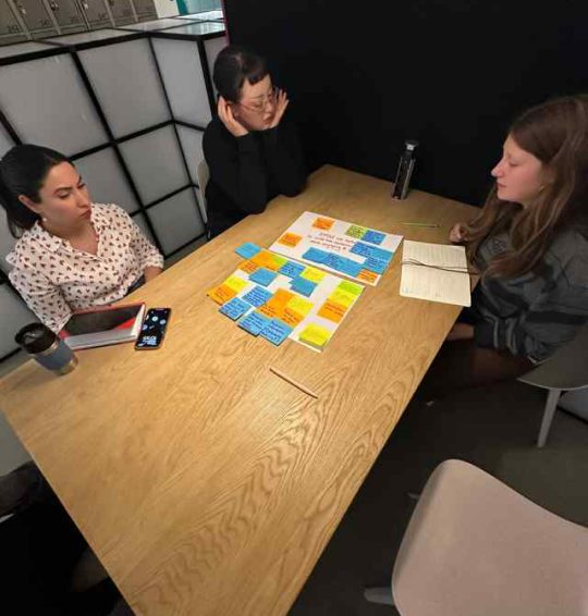 Maryam and two teammates around a table covered in sticky notes during an ideation workshop