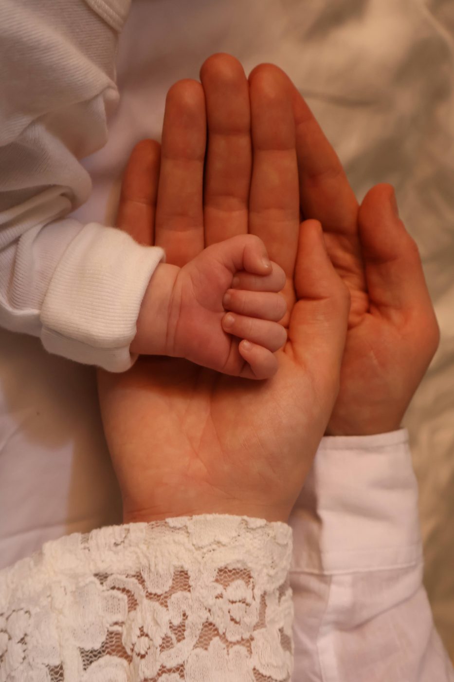 A baby's hand resting in two adult hands